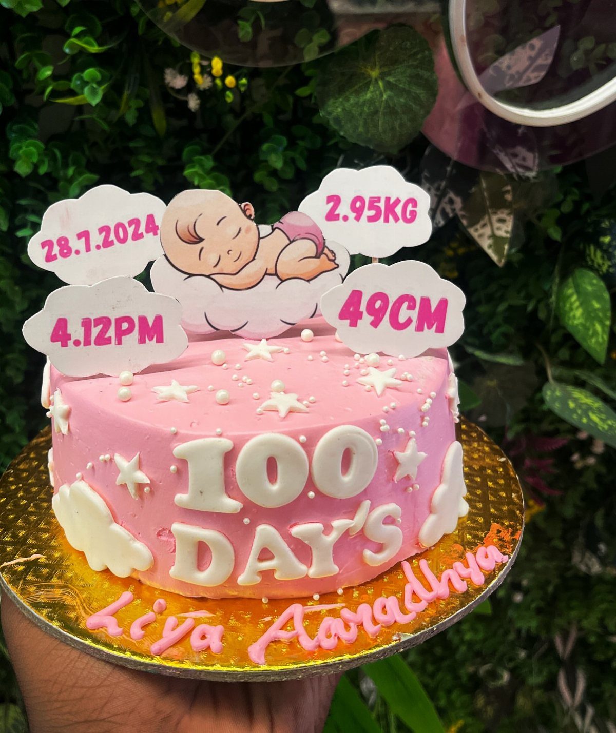 Pink 100 day celebration cake with baby details on cloud toppers and stars.