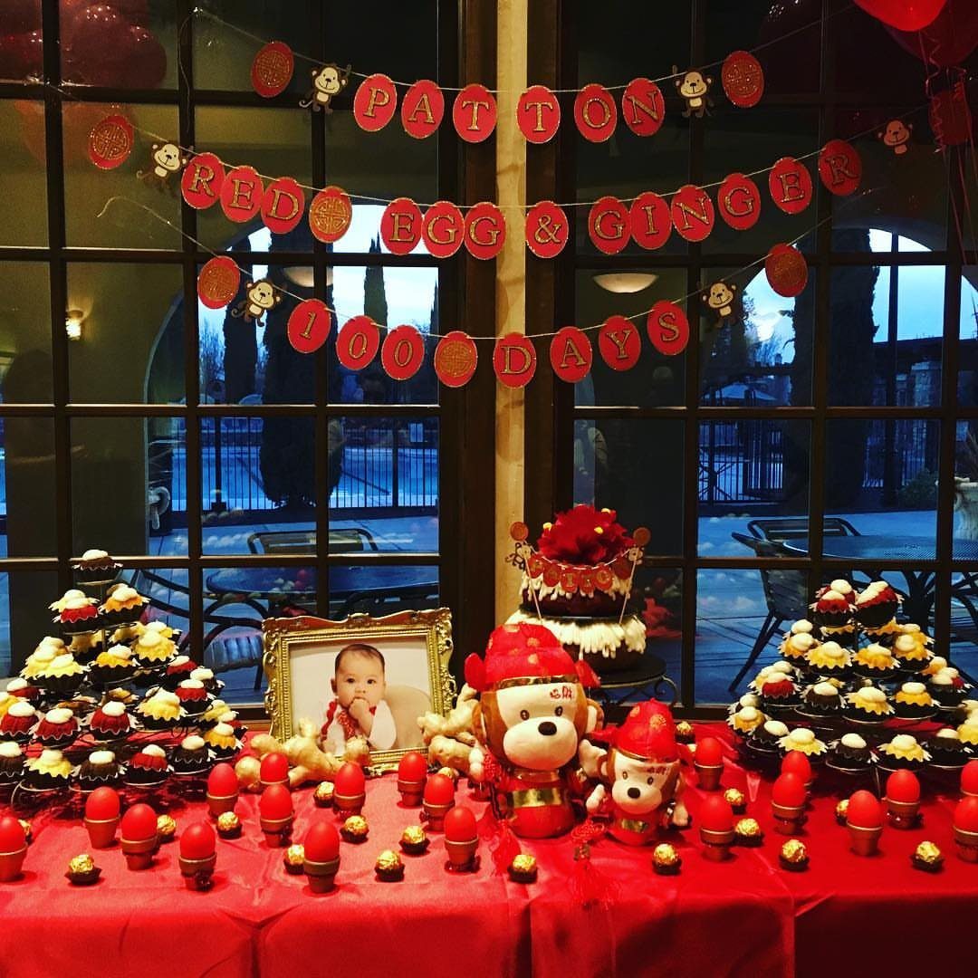 Celebration table with red eggs, ginger, cupcakes, and 100 days banners.