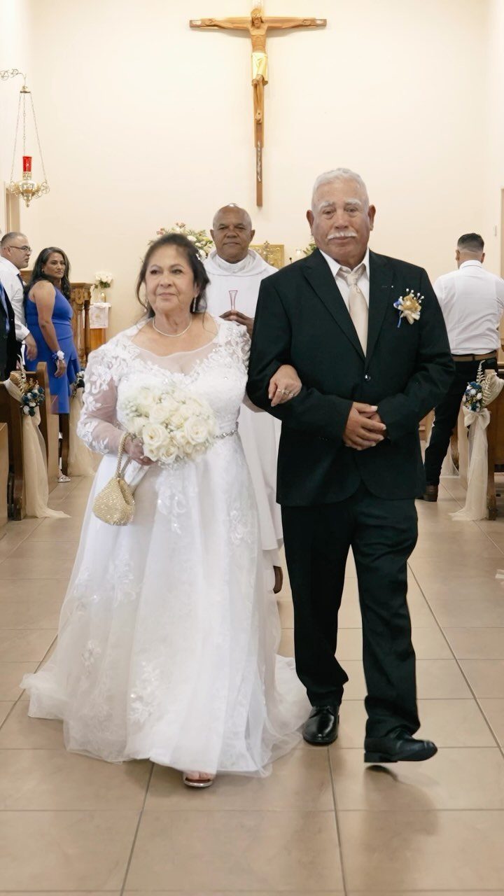 Older couple in wedding attire walking arm-in-arm inside a church during a ceremony
