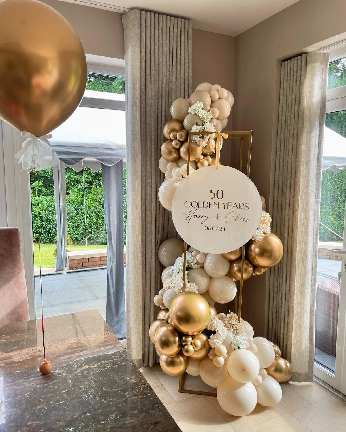 Gold and white balloon arch with a 50th anniversary sign for Harry and Chris.