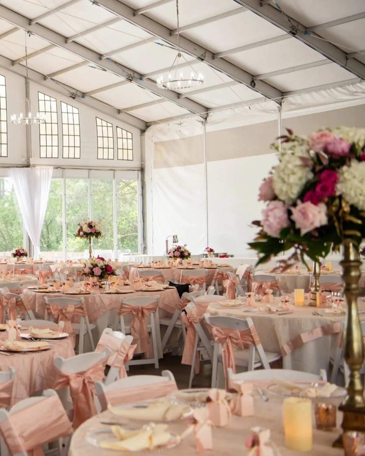 Event tent with round tables, pink ribbons on chairs, and floral centerpieces.
