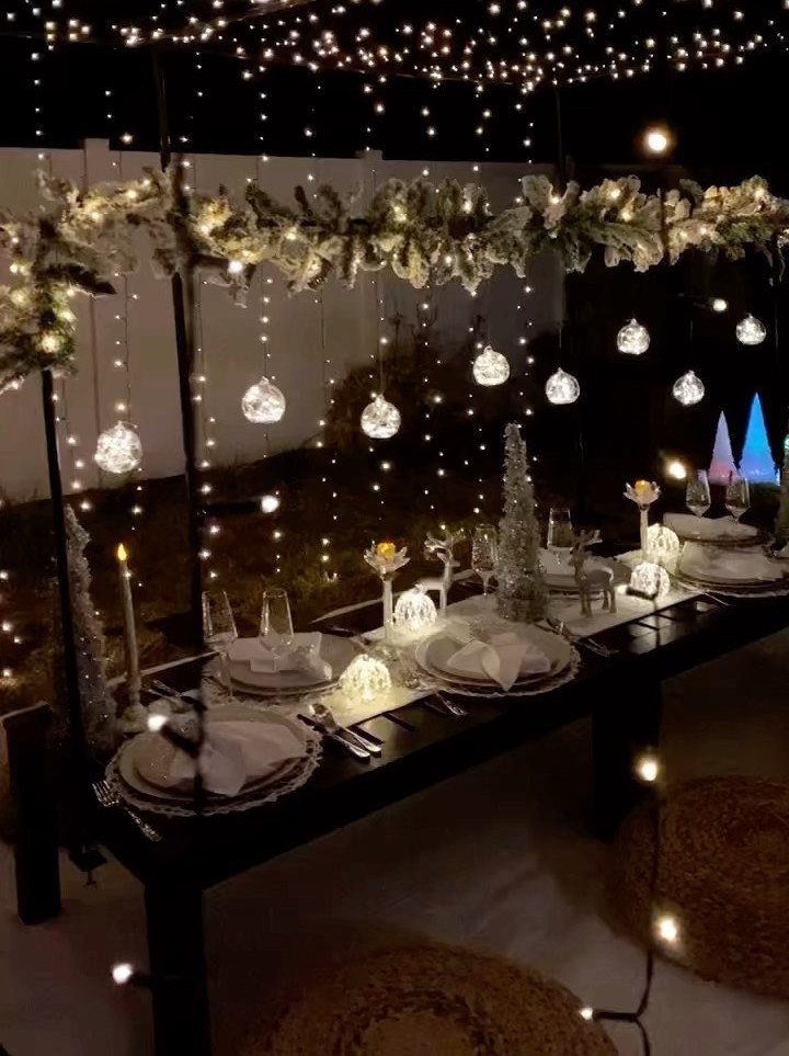 Outdoor dinner table set at night with fairy lights and white decorations