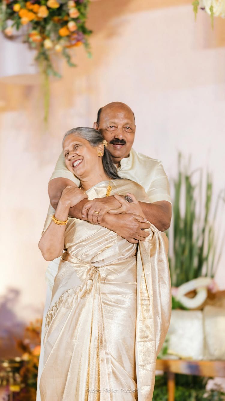 Older Indian couple embracing and smiling, woman wearing a shimmering gold saree.