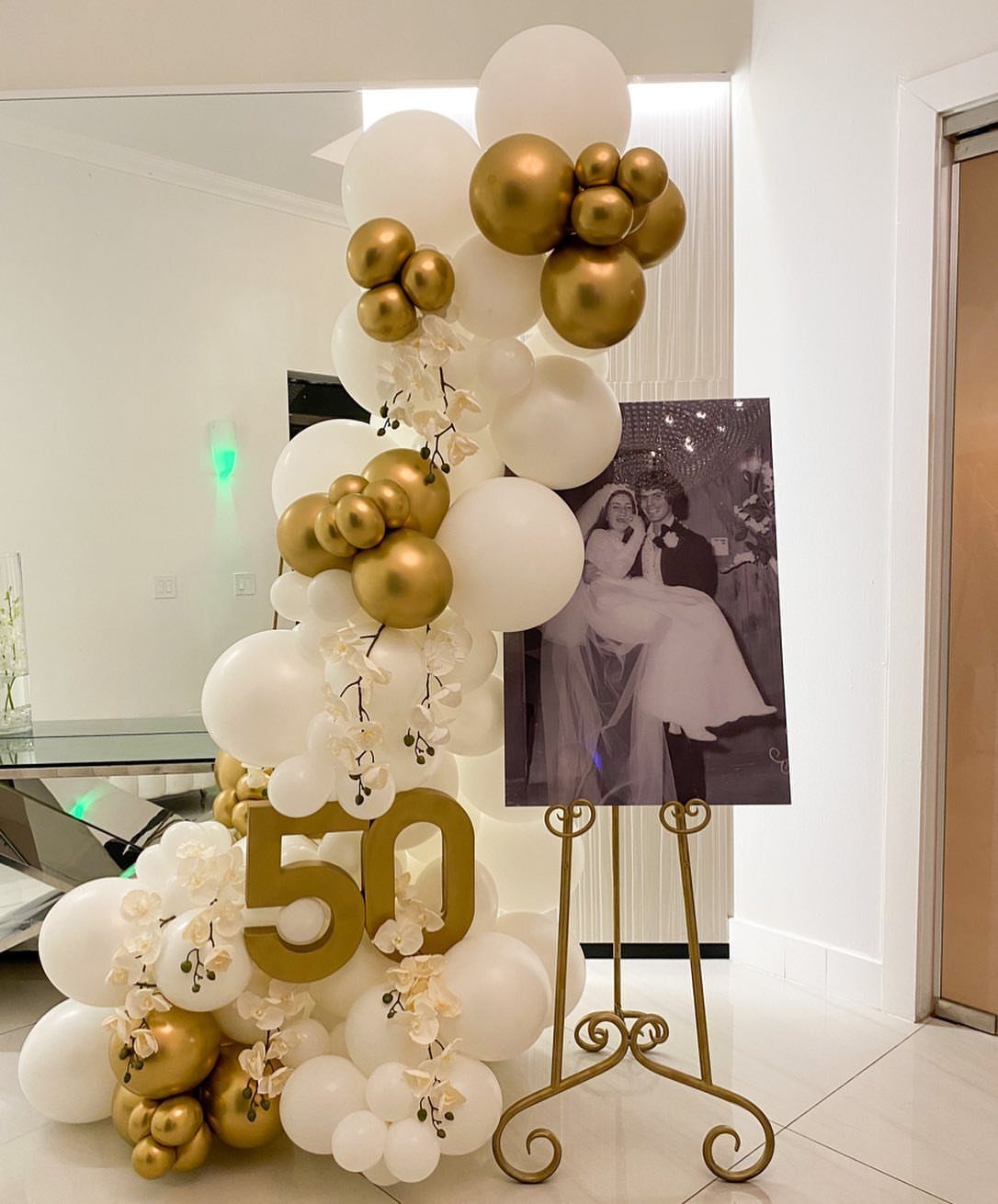 Gold and white balloon arch with number 50 and wedding photo on easel