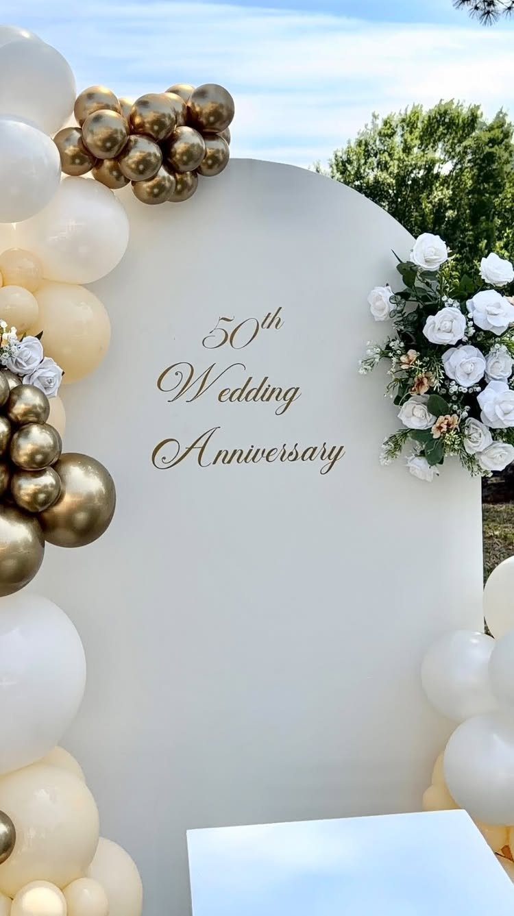 White arched backdrop with gold 50th anniversary text, gold balloons, and white roses.