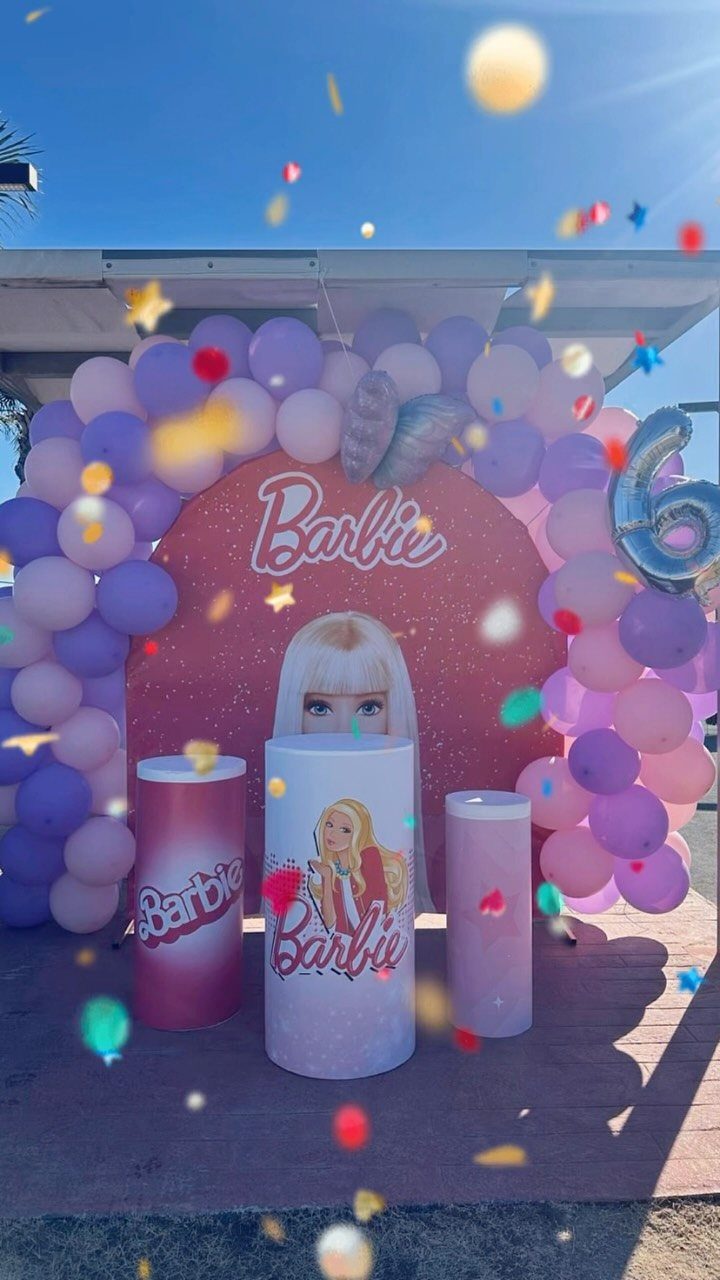 Barbie themed party setup with pink backdrop, purple balloon arch, and branded pedestals.