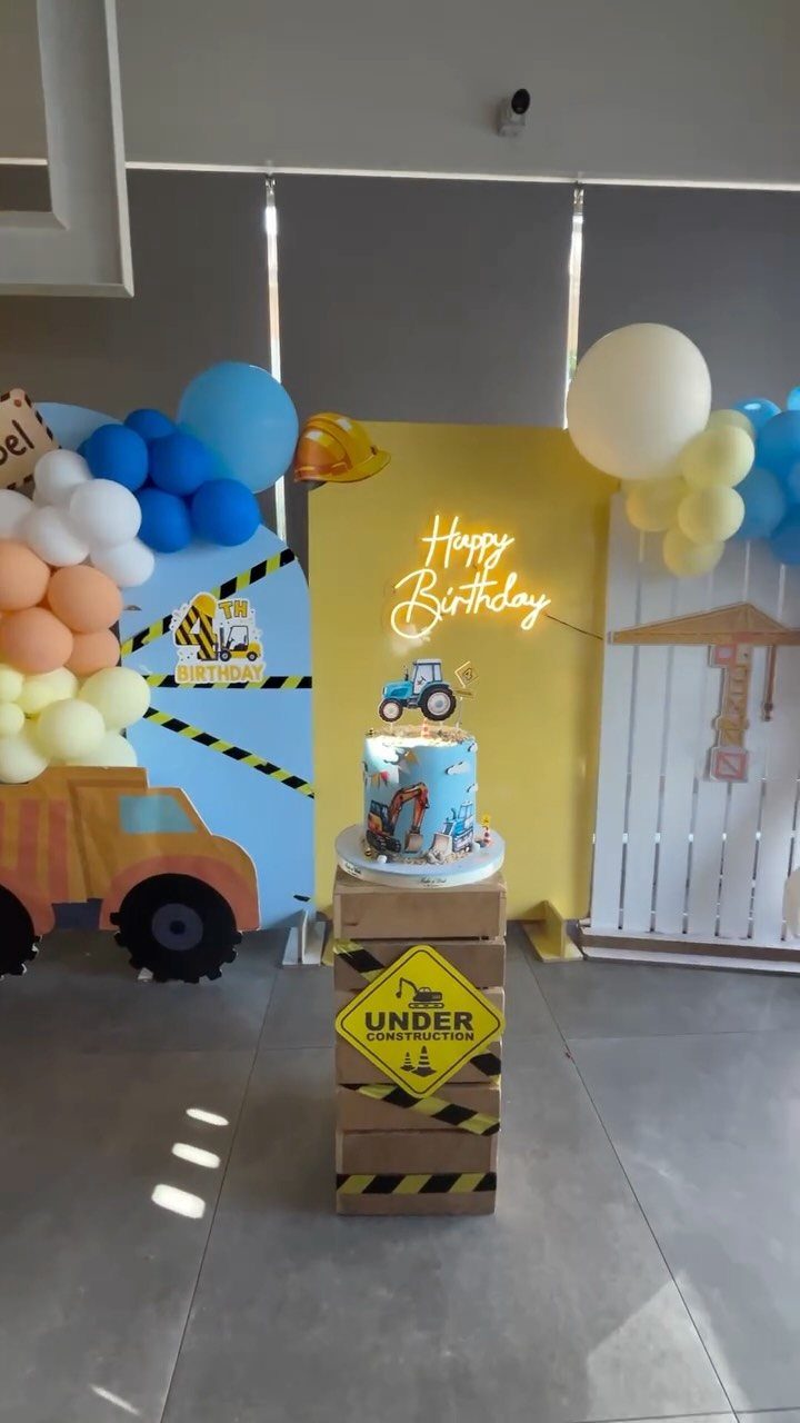Construction themed birthday party setup with a cake on crates and colorful balloons.