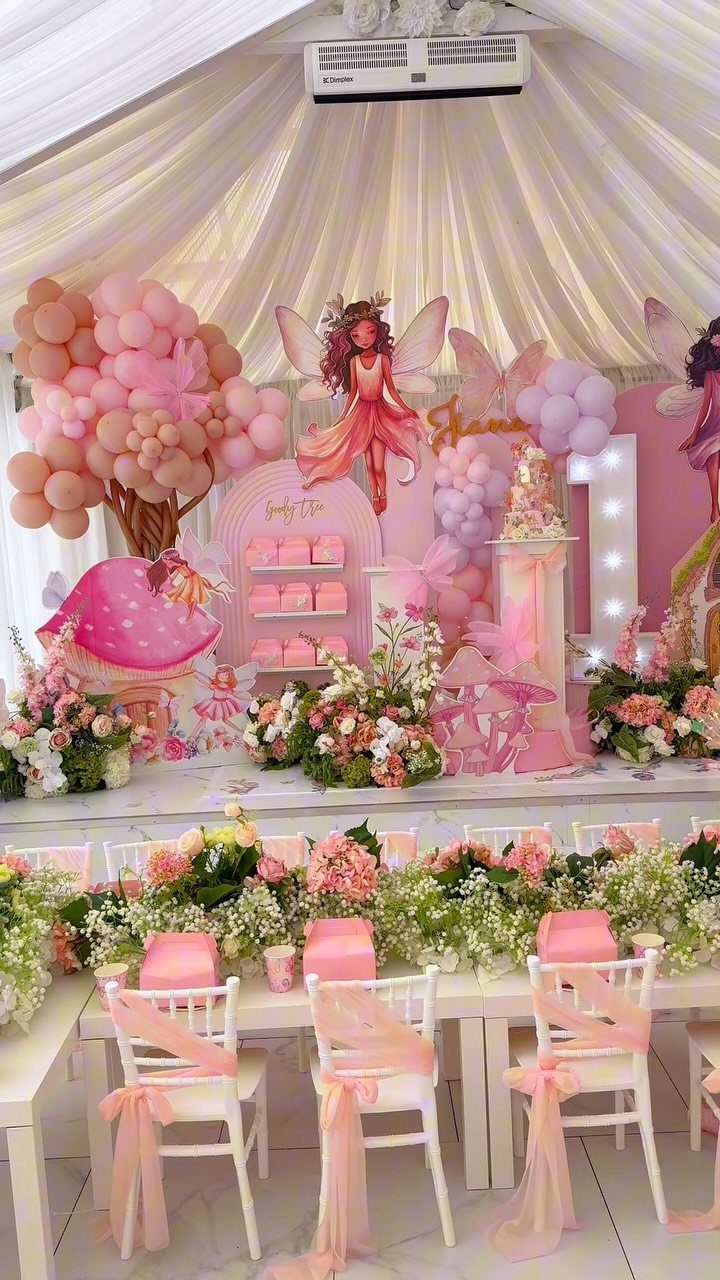 Pink fairy themed party setup with balloons, flowers, and a fairy cutout.