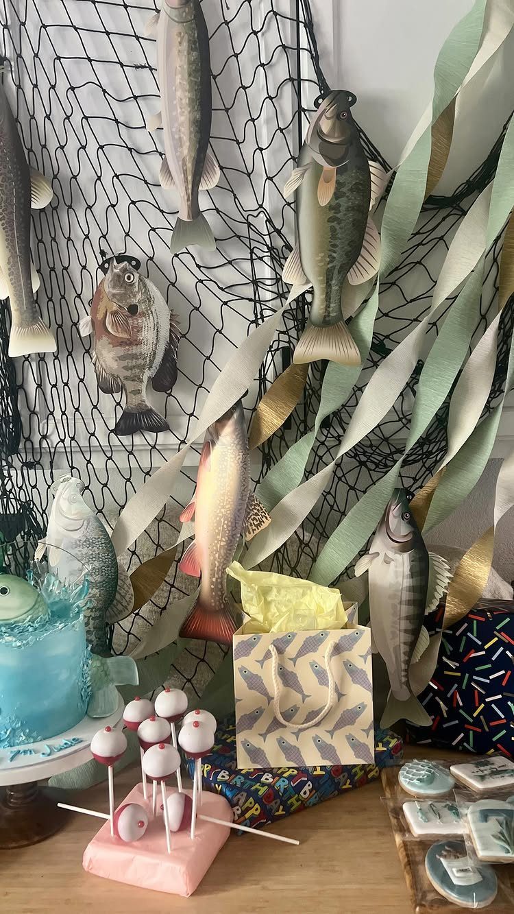 Fishing party decorations with a net backdrop, fish figures, blue cake, and treats.