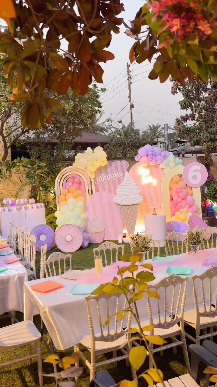 Pastel party decorations featuring a large ice cream cone and colorful balloons outdoors.