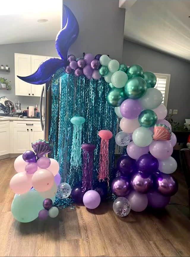 Mermaid tail balloon and balloon arch with teal tinsel backdrop and jellyfish decorations.