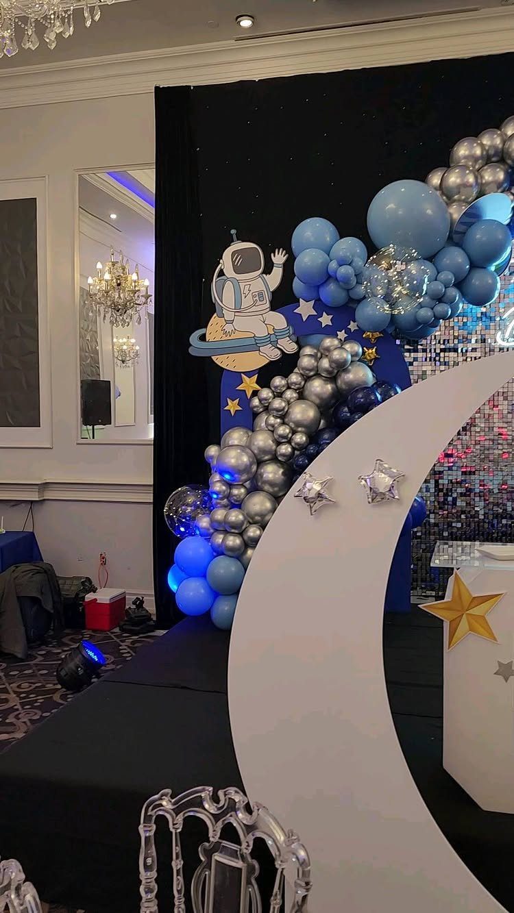 Outer space party decorations featuring blue balloons, a white crescent moon, and an astronaut.