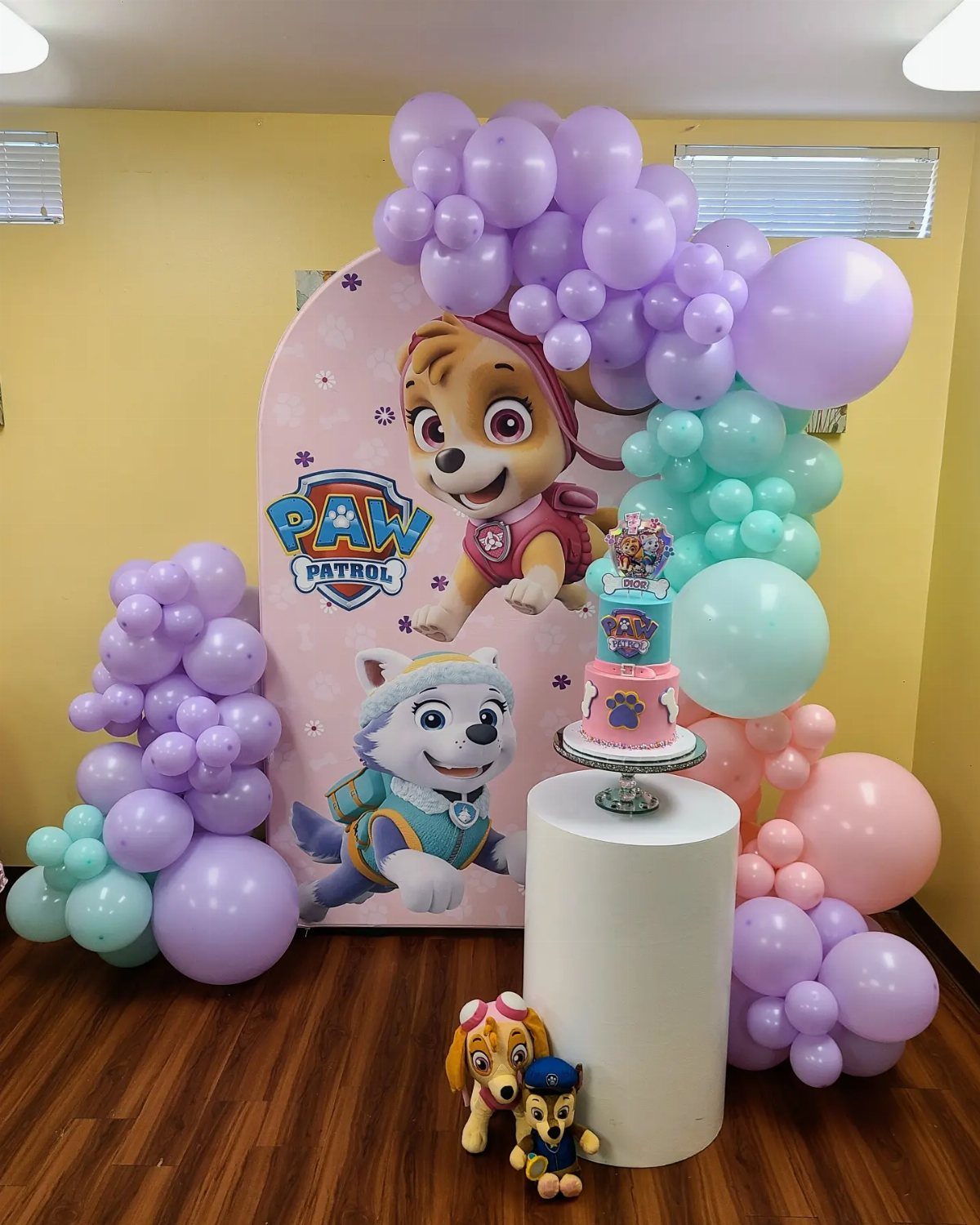 Paw Patrol party setup with character backdrop, colorful balloon arches, and tiered cake.