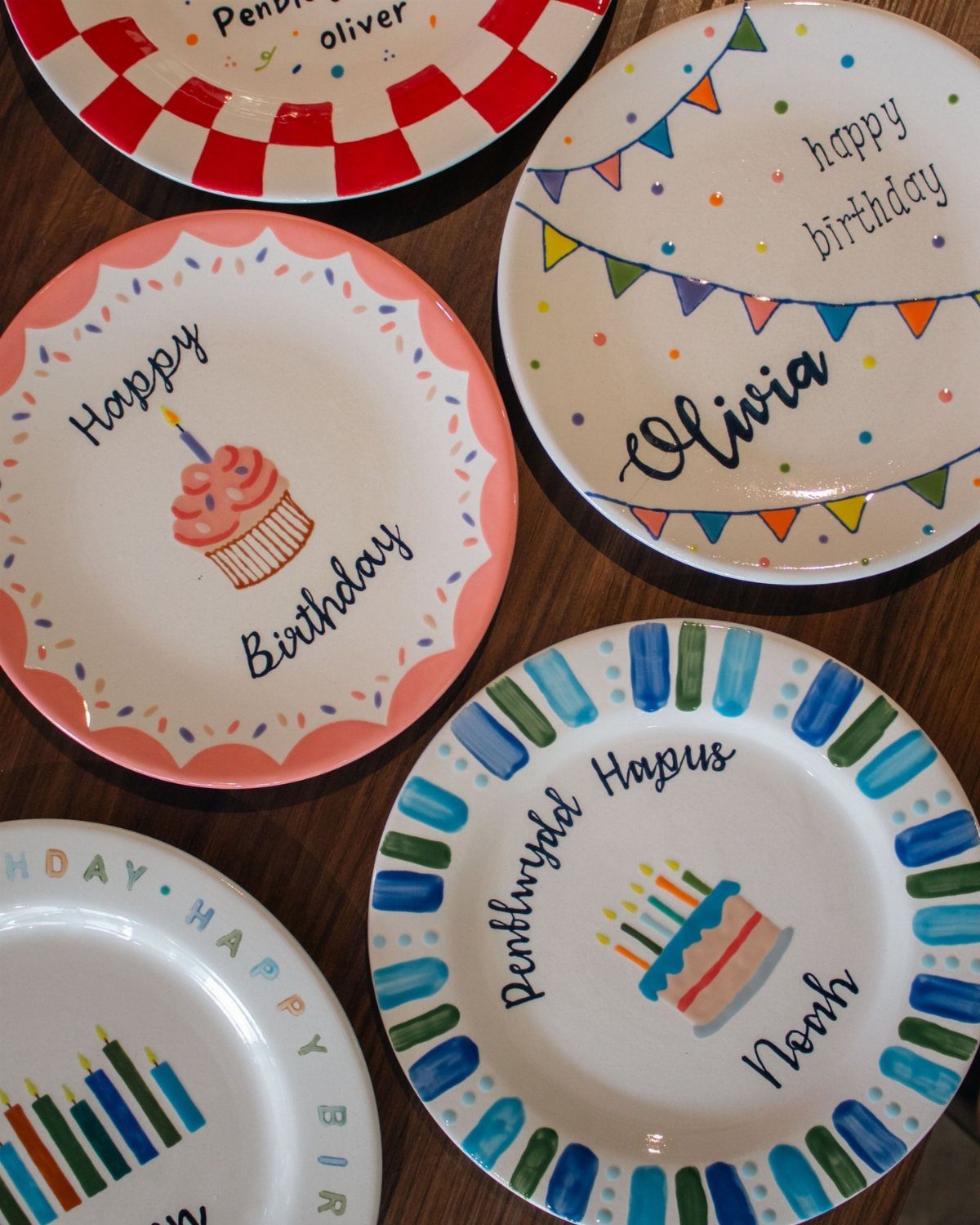 Hand-painted ceramic birthday plates with colorful cakes, bunting, and personalized names.