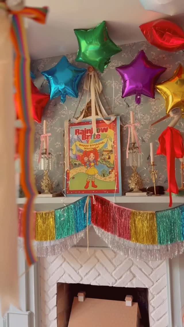Colorful star balloons and a rainbow tinsel banner decorating a white fireplace mantel.