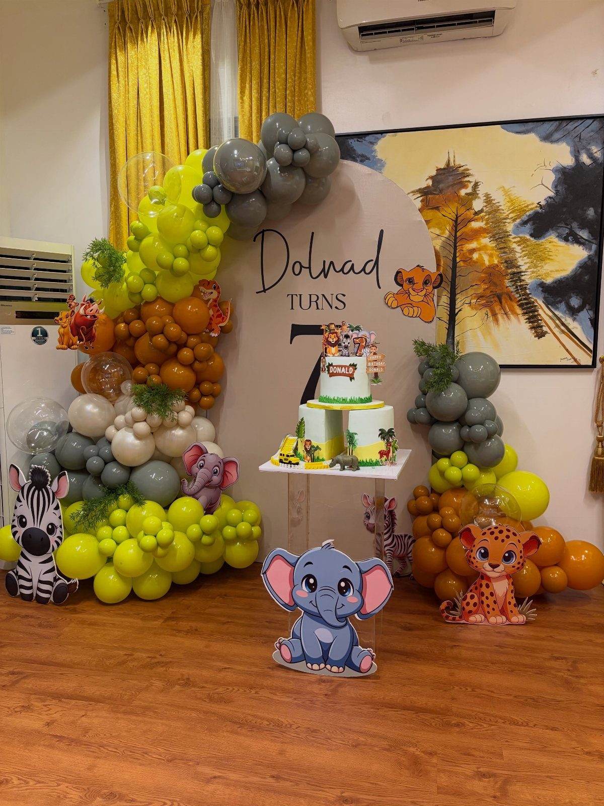 Safari party decorations with animal cutouts, a themed cake, and colorful balloon arches.