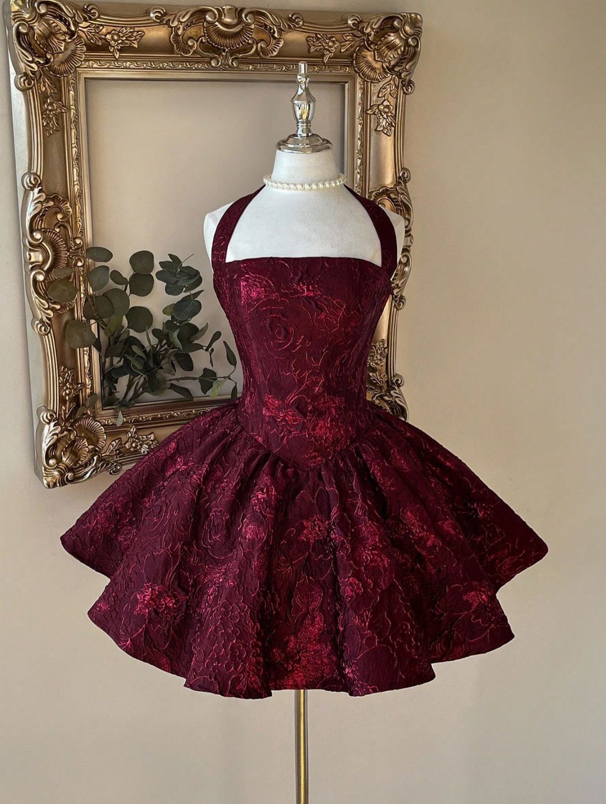 Burgundy brocade cocktail dress on a mannequin with a gold ornate frame background
