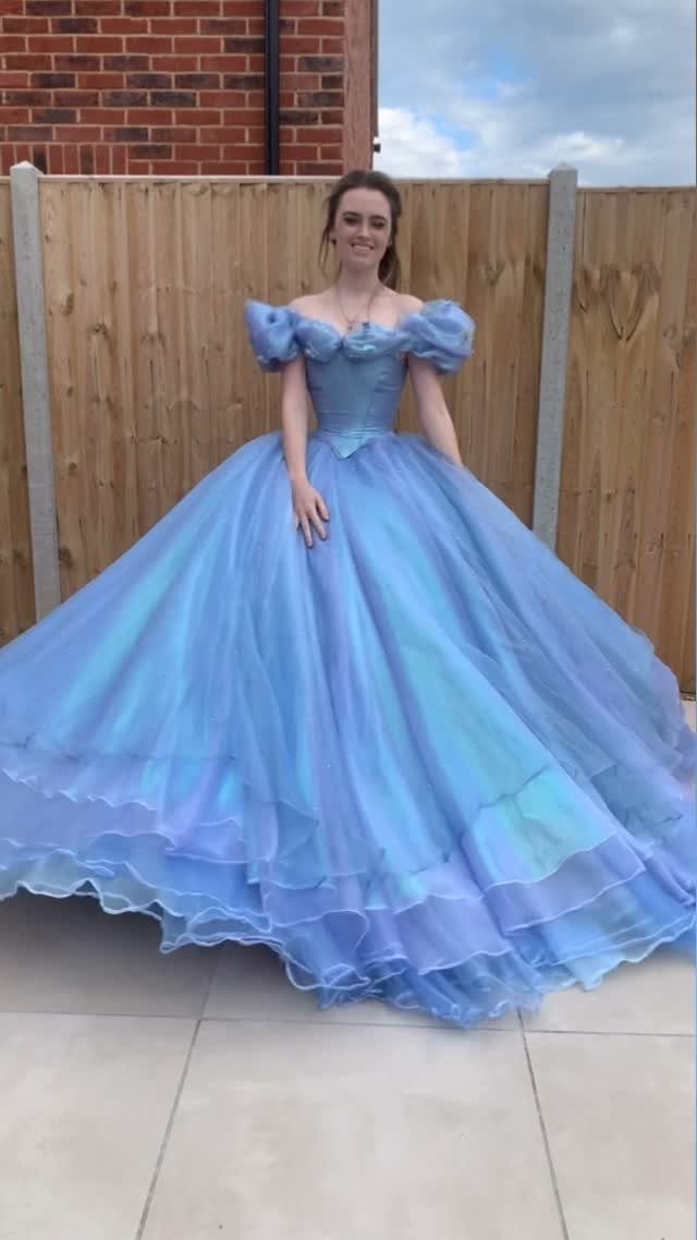 Woman in a voluminous light blue ballgown with puffed sleeves standing by a fence