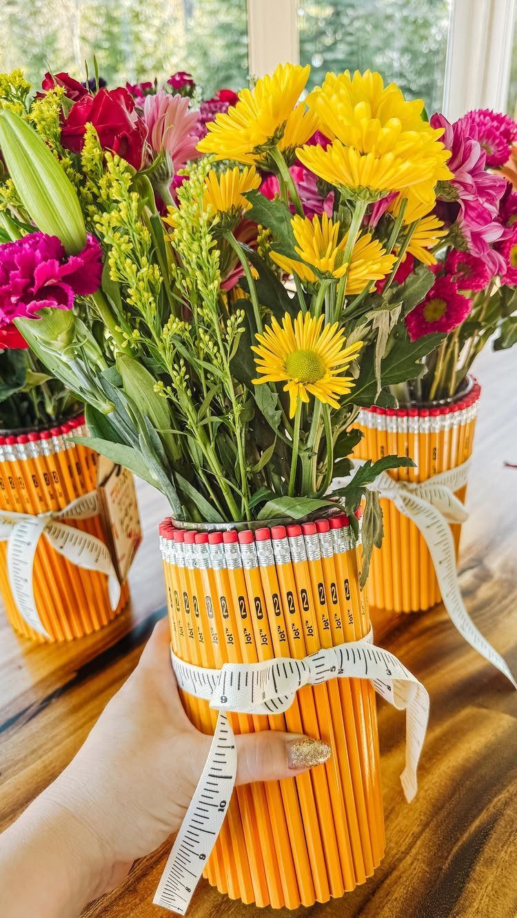 Pencil vase tied with measuring tape ribbon holding yellow and pink flowers.