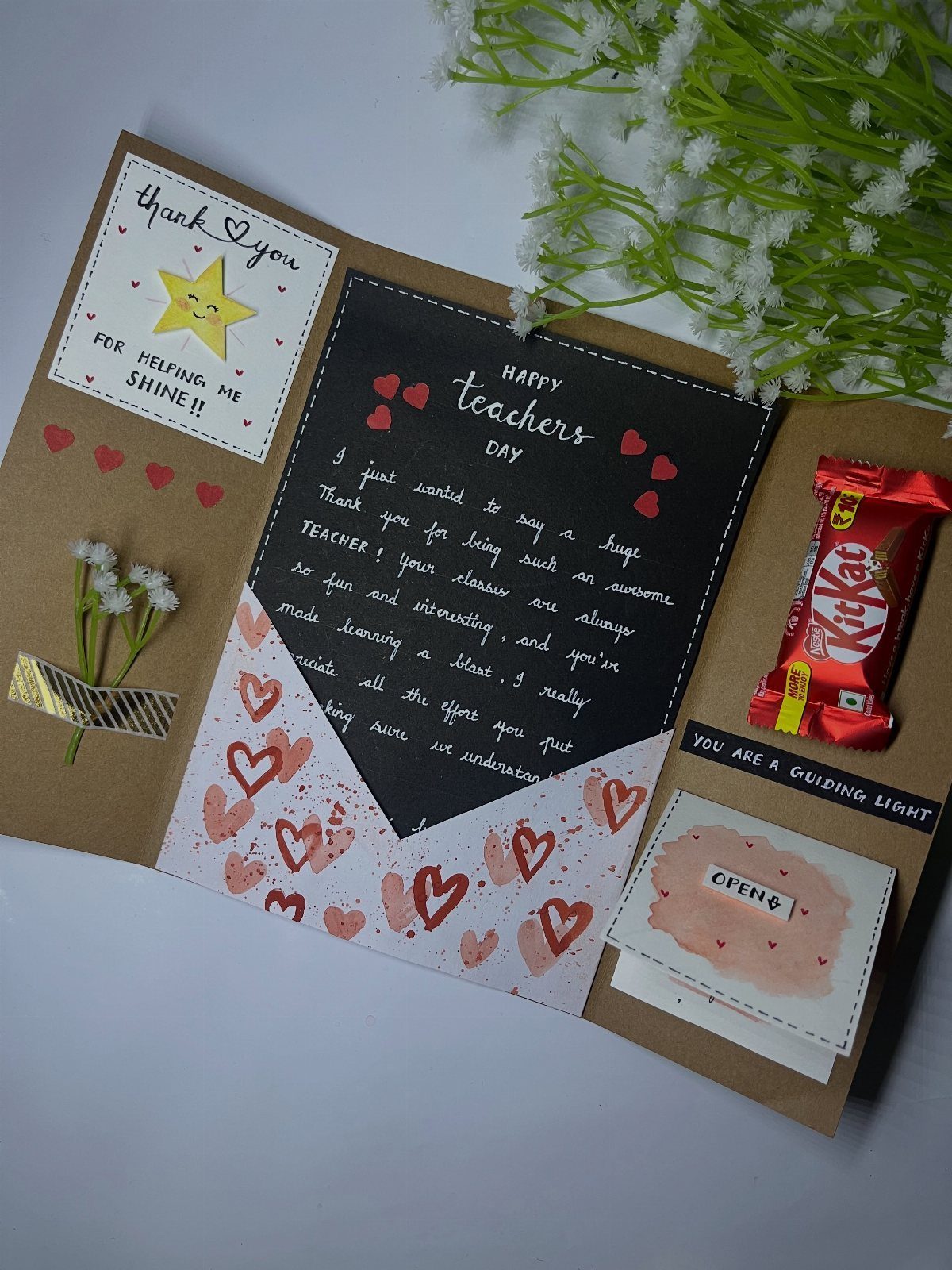 Handmade teacher's day card with a handwritten note, KitKat bar, and small flowers.