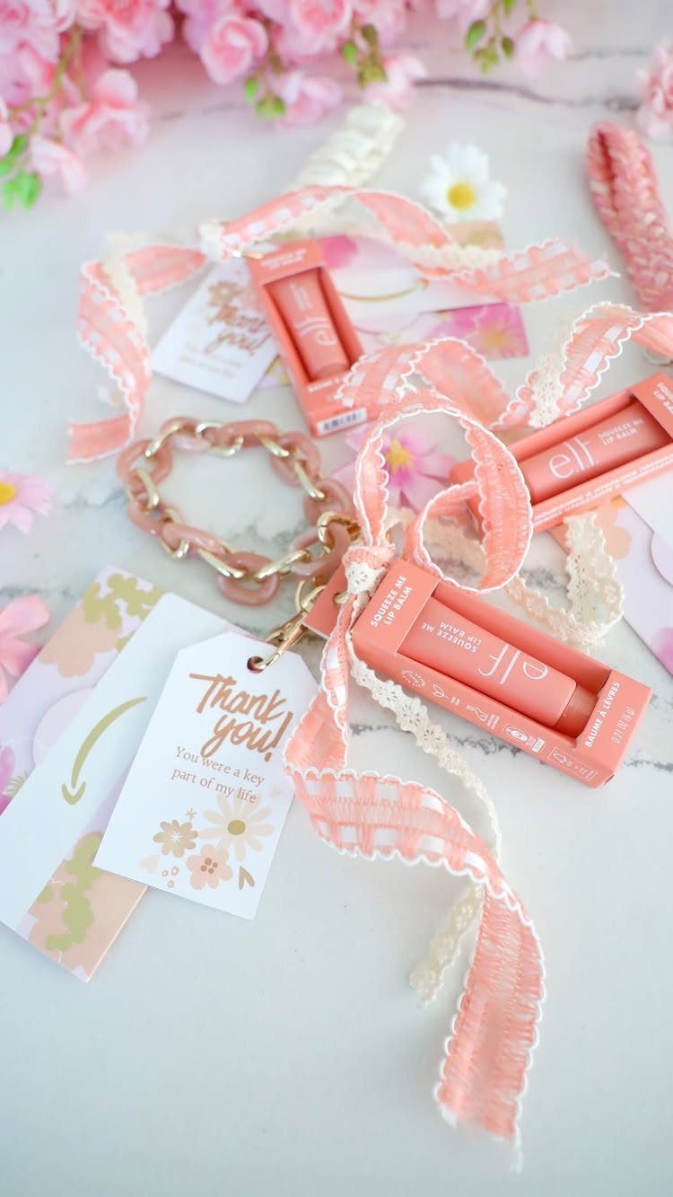 Pink lip glosses and ribbons with a thank you tag on white surface.