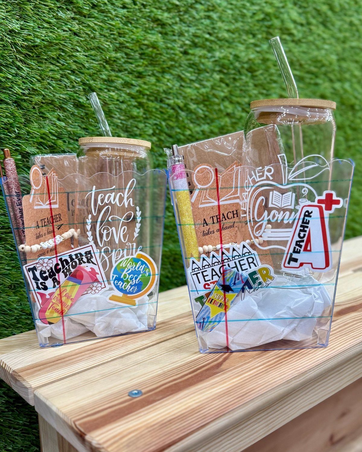 Two clear gift baskets with teacher-themed stationery, tumblers, and treats on wood.