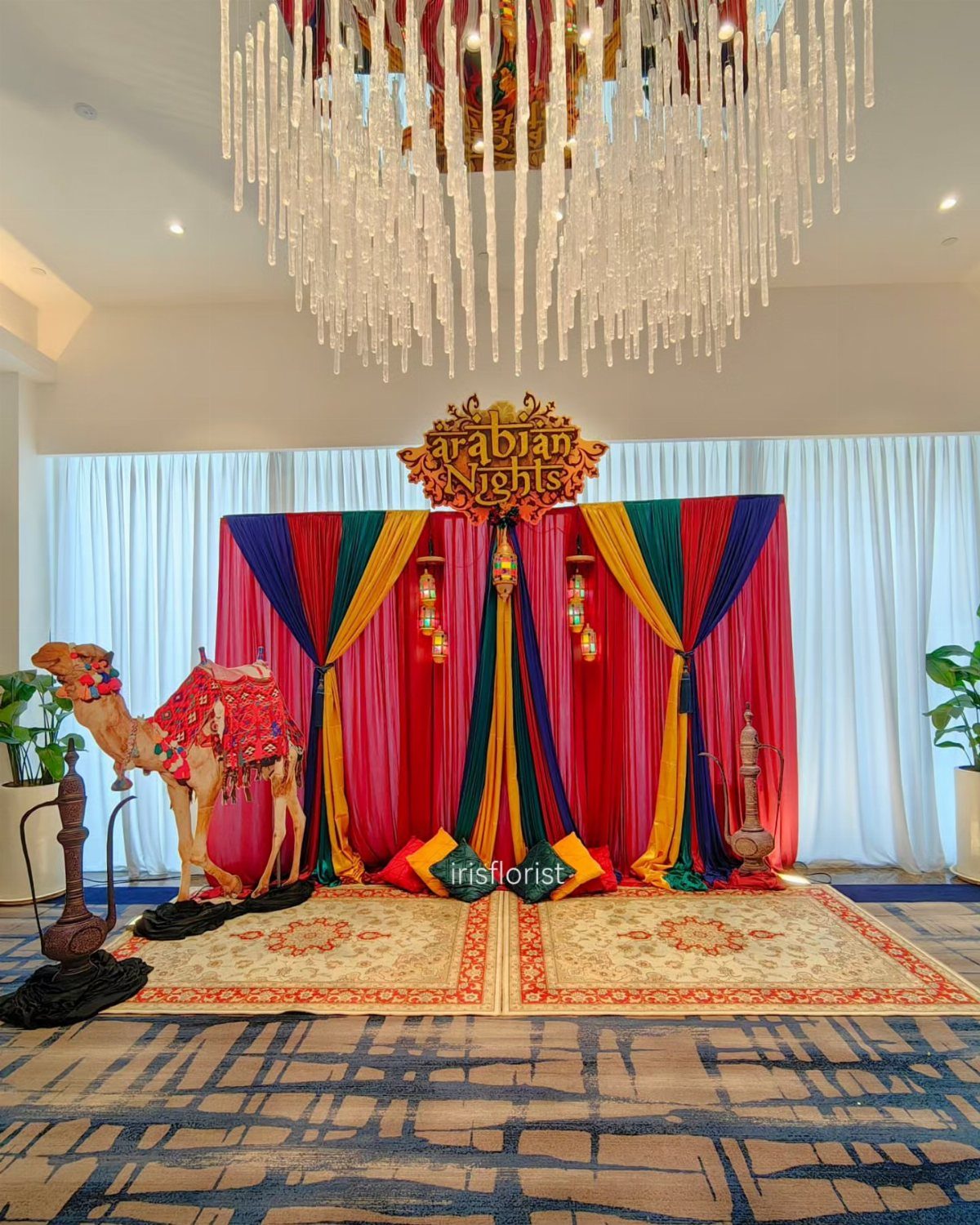 Arabian Nights themed photo backdrop with colorful drapery, camel statue, and ornate rugs.