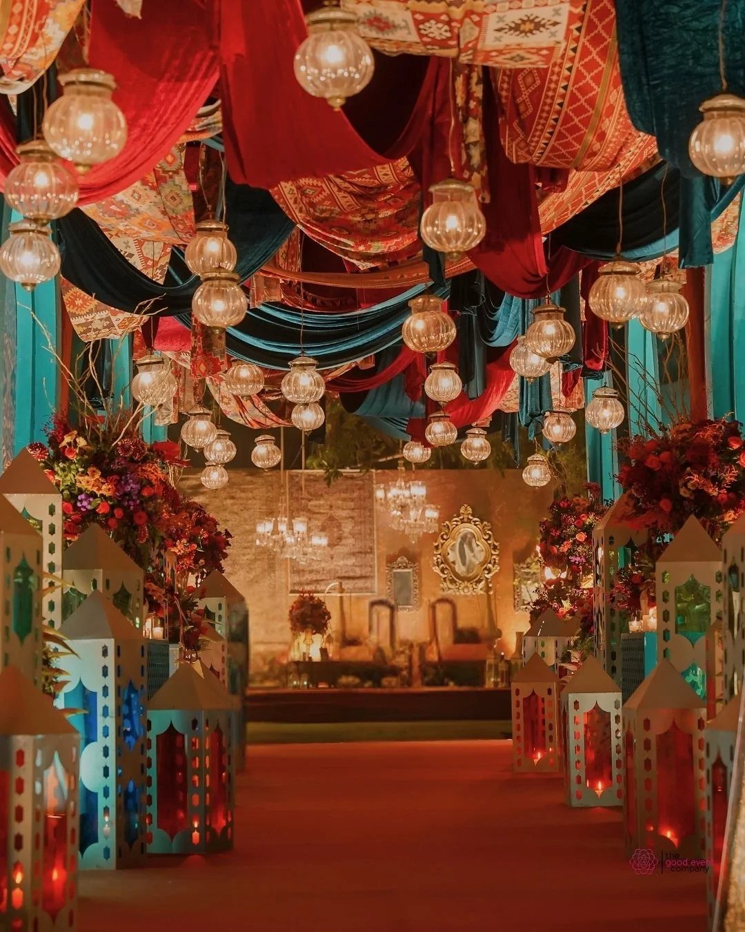 Red and teal draped fabrics with hanging lanterns over a red carpet path
