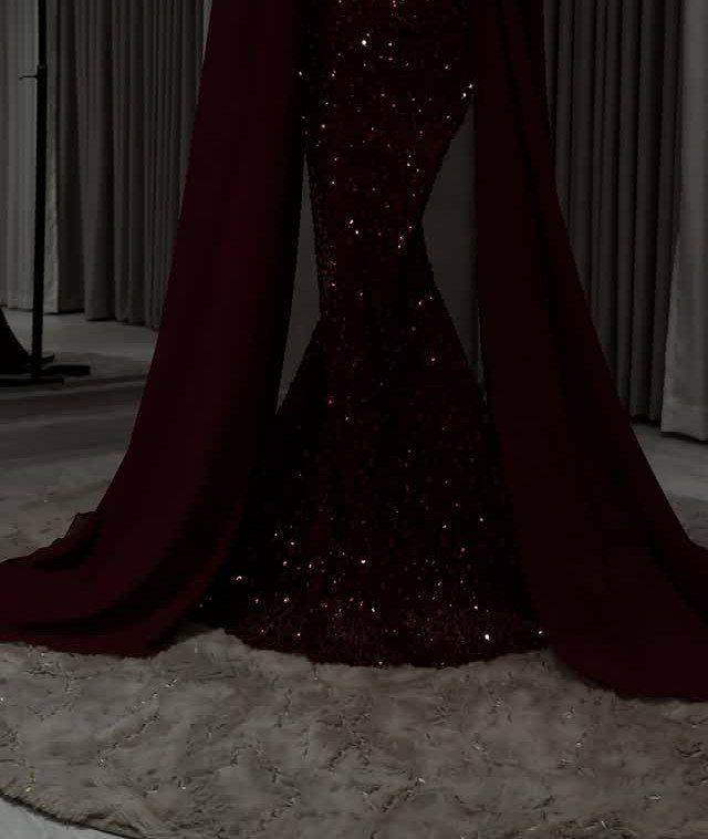 Dark red sequined gown with a long flowing cape on a grey rug