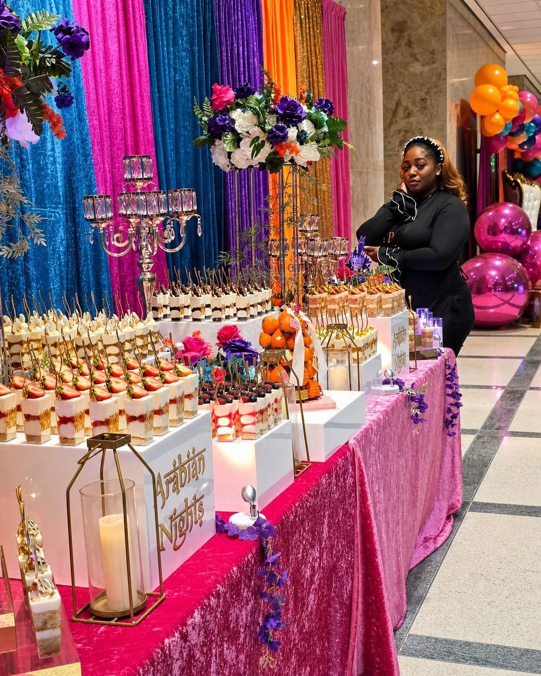 Dessert table with pink velvet cloth and colorful curtains for Arabian Nights theme.