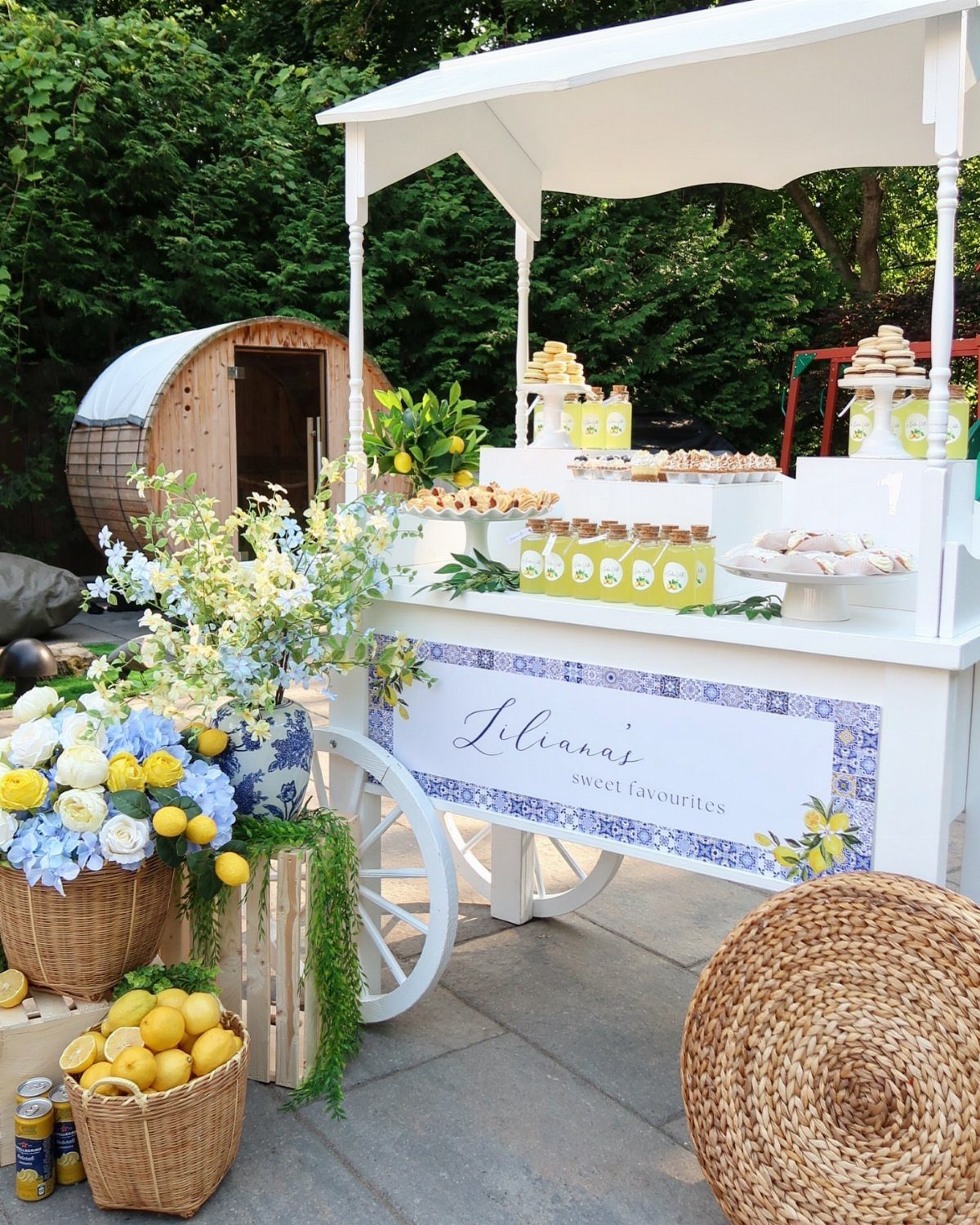 White vintage dessert cart with yellow treats and blue flowers in a garden.