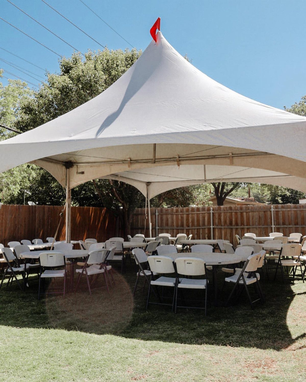 White event tent with round tables and chairs on a grassy backyard lawn.