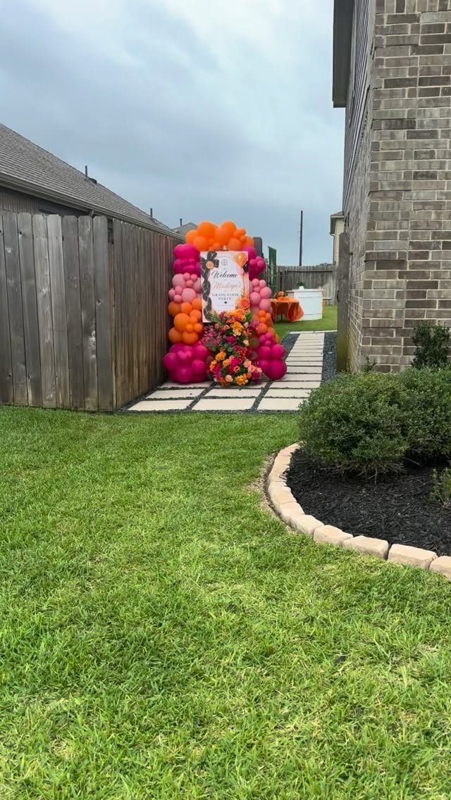 Balloon arch with pink and orange balloons surrounding a welcome sign in a backyard