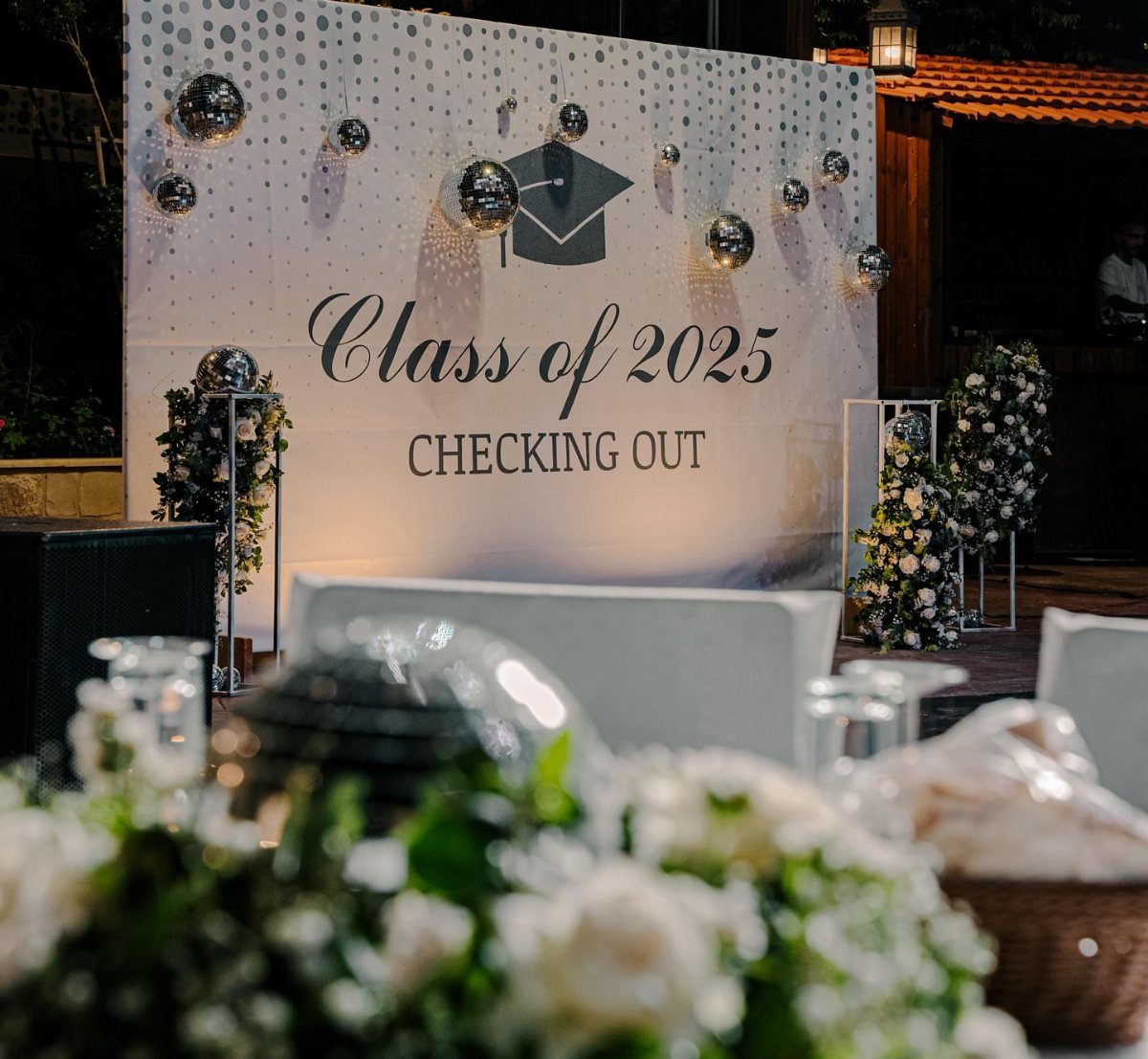 Graduation photo booth backdrop with Class of 2025 text, disco balls, and white flowers.