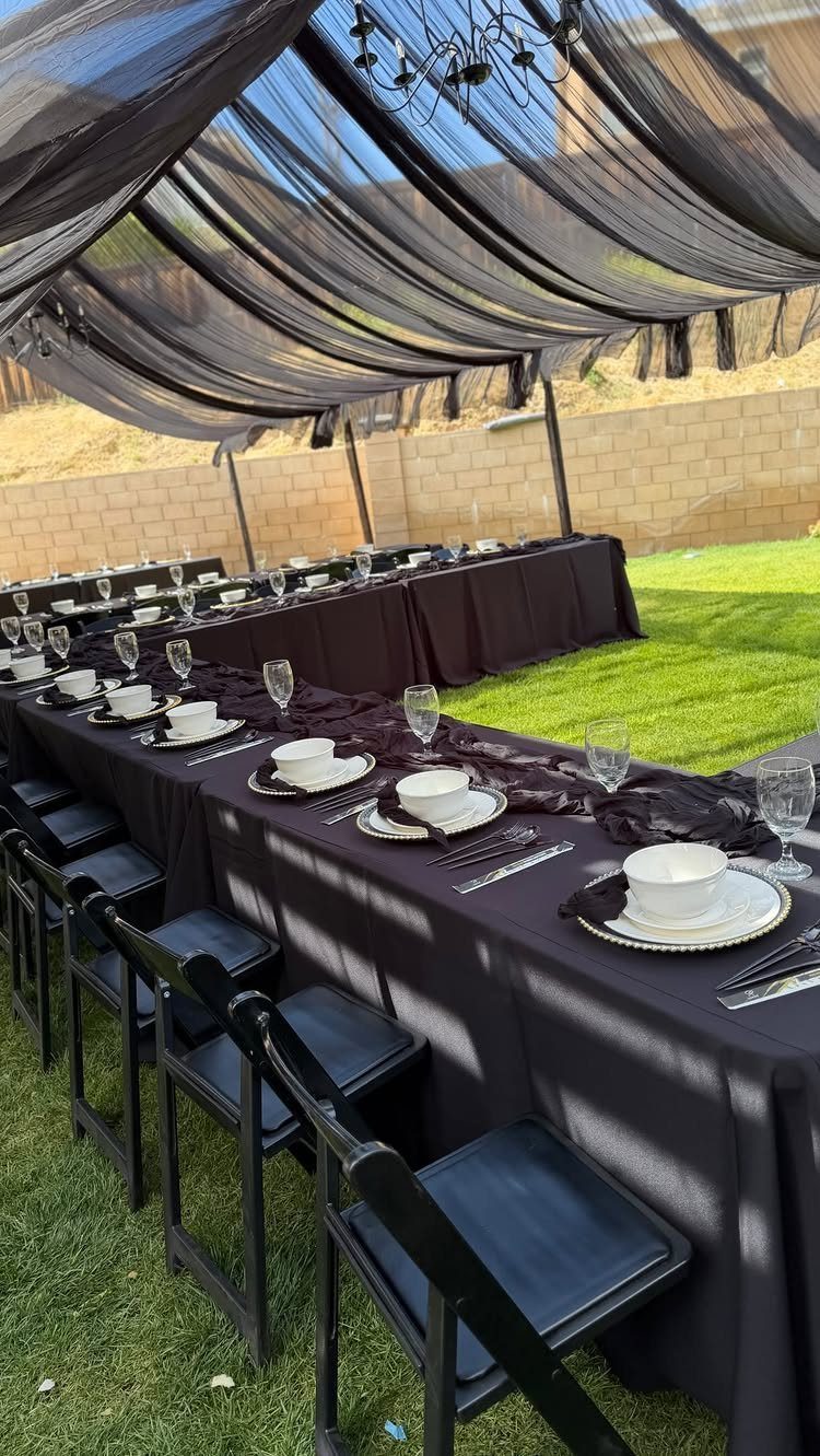 Long dining table with black linens under a draped black sheer fabric canopy.