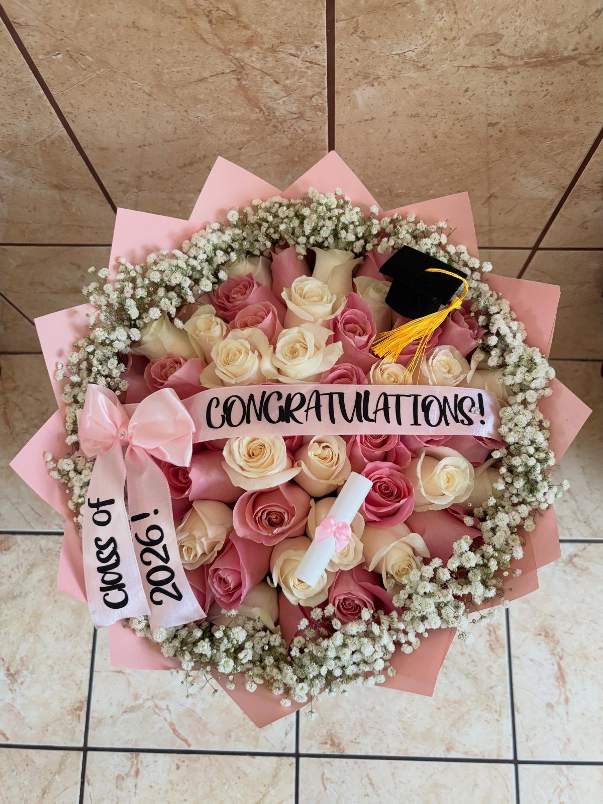 Bouquet of pink and white roses with a graduation cap and diploma.