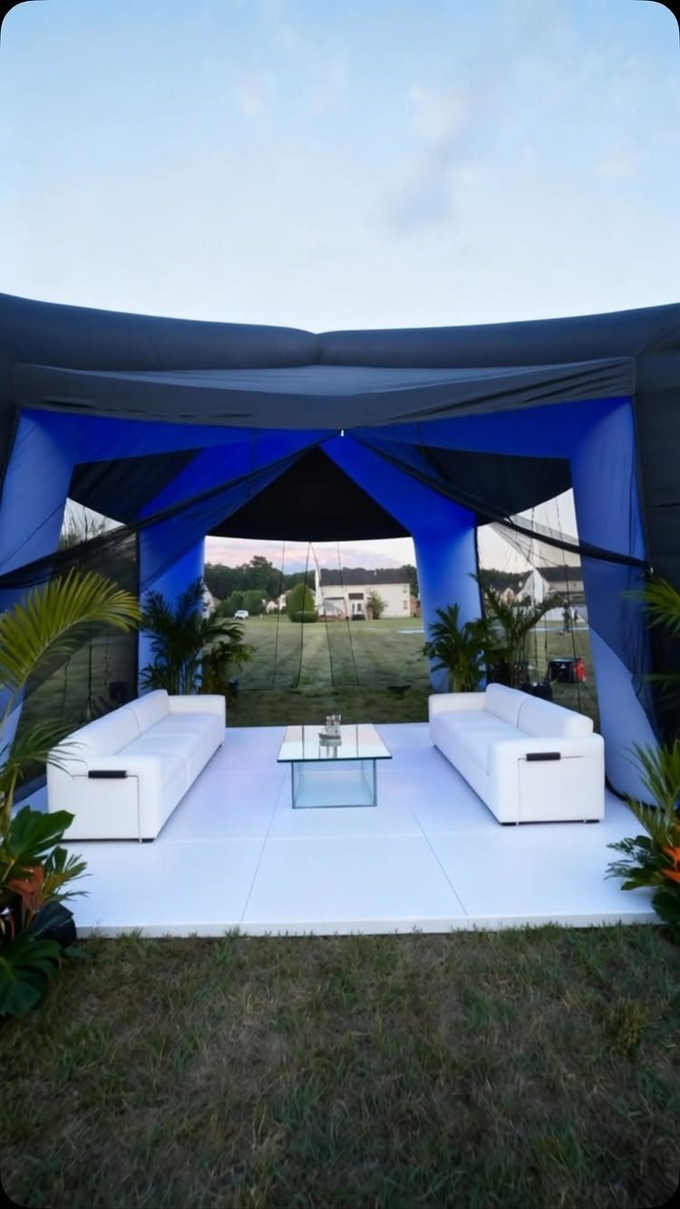 Blue and black outdoor lounge tent with white sofas and a glass table.