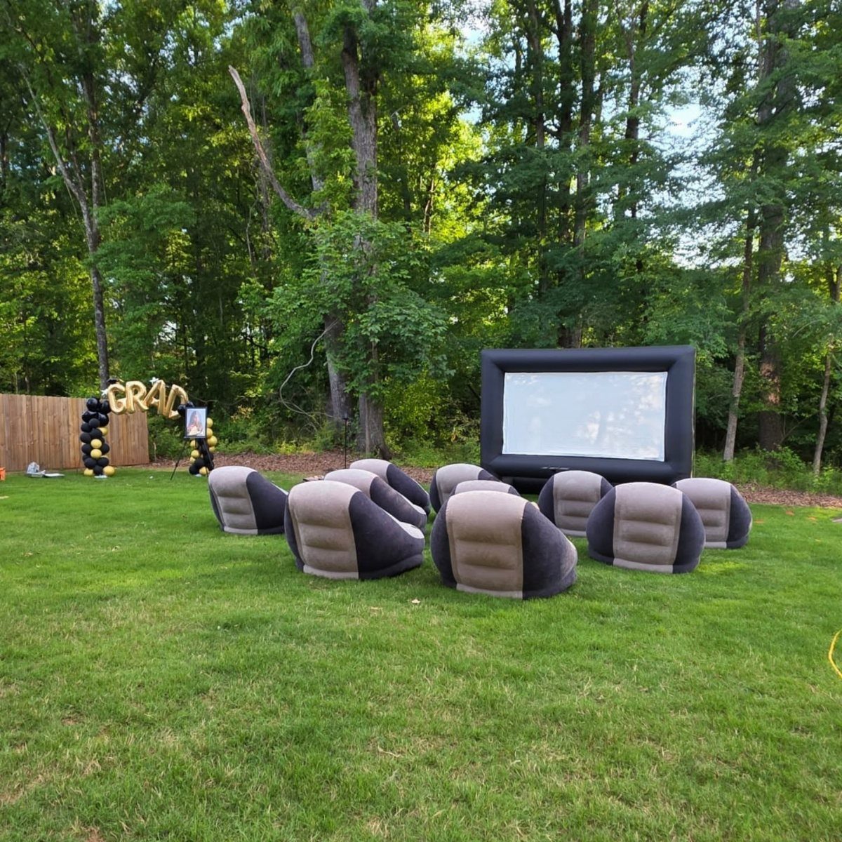 Inflatable movie screen and bean bag chairs on a lawn with graduation balloons.