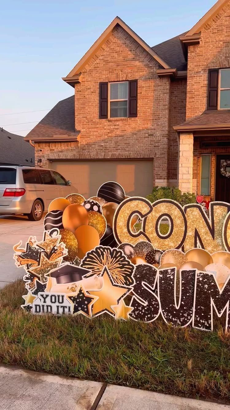 Gold and black glittery graduation yard signs on a lawn in front of a house.