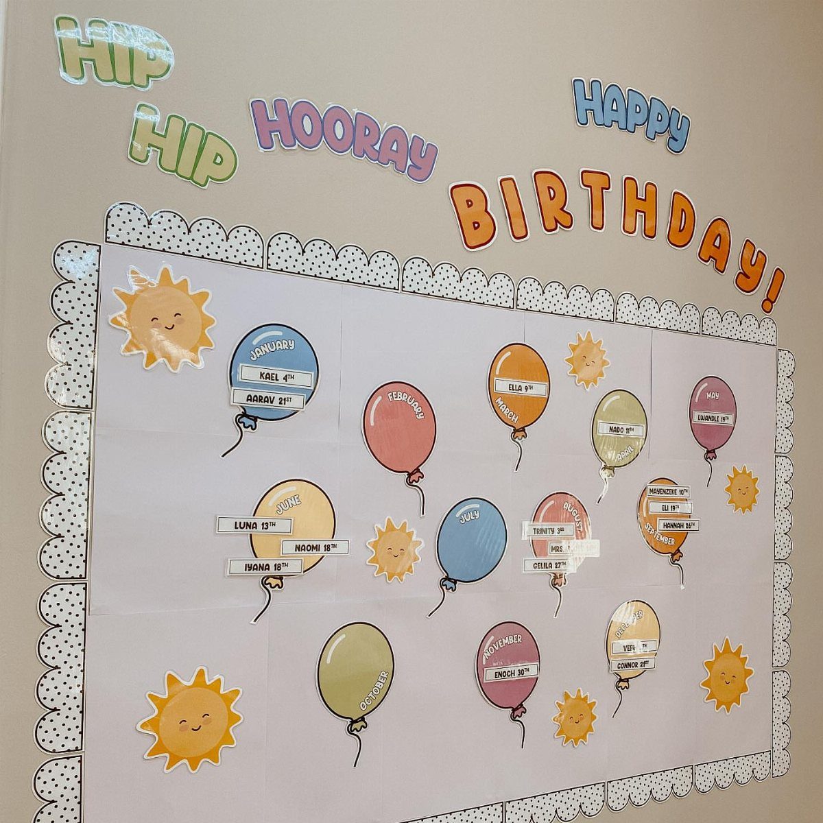 Birthday board classroom display with colorful paper balloons and suns on a wall