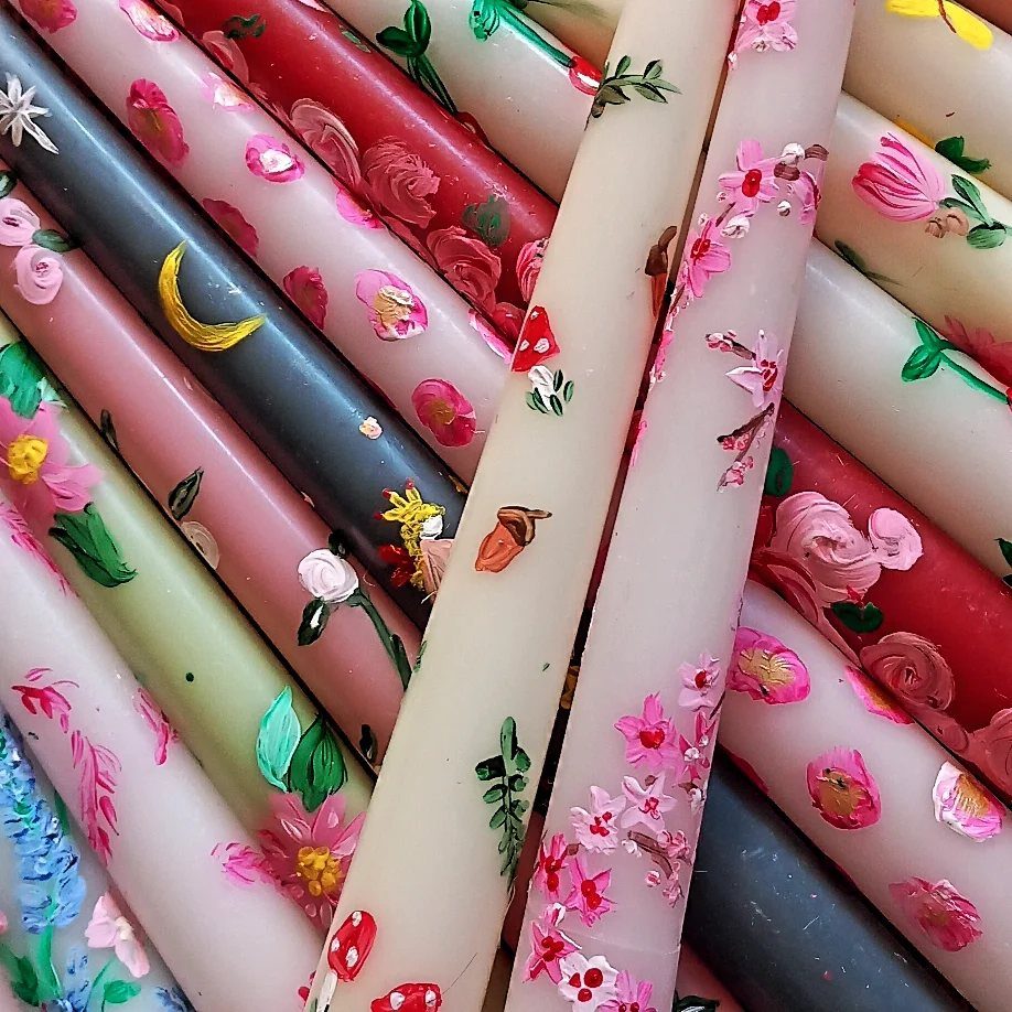 Hand-painted tapered candles in various colors featuring colorful floral and celestial designs.