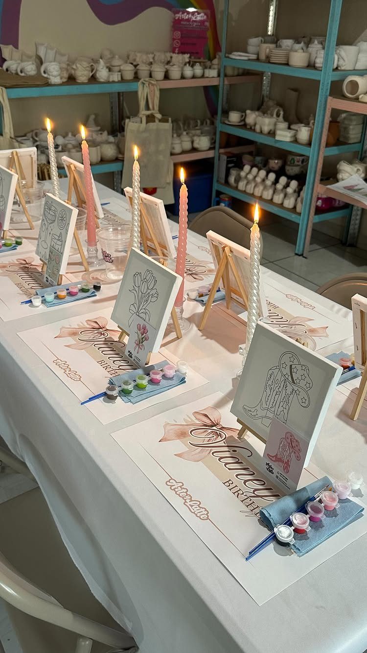 Painting stations with small canvases, paint palettes, and lit candles on a white table.