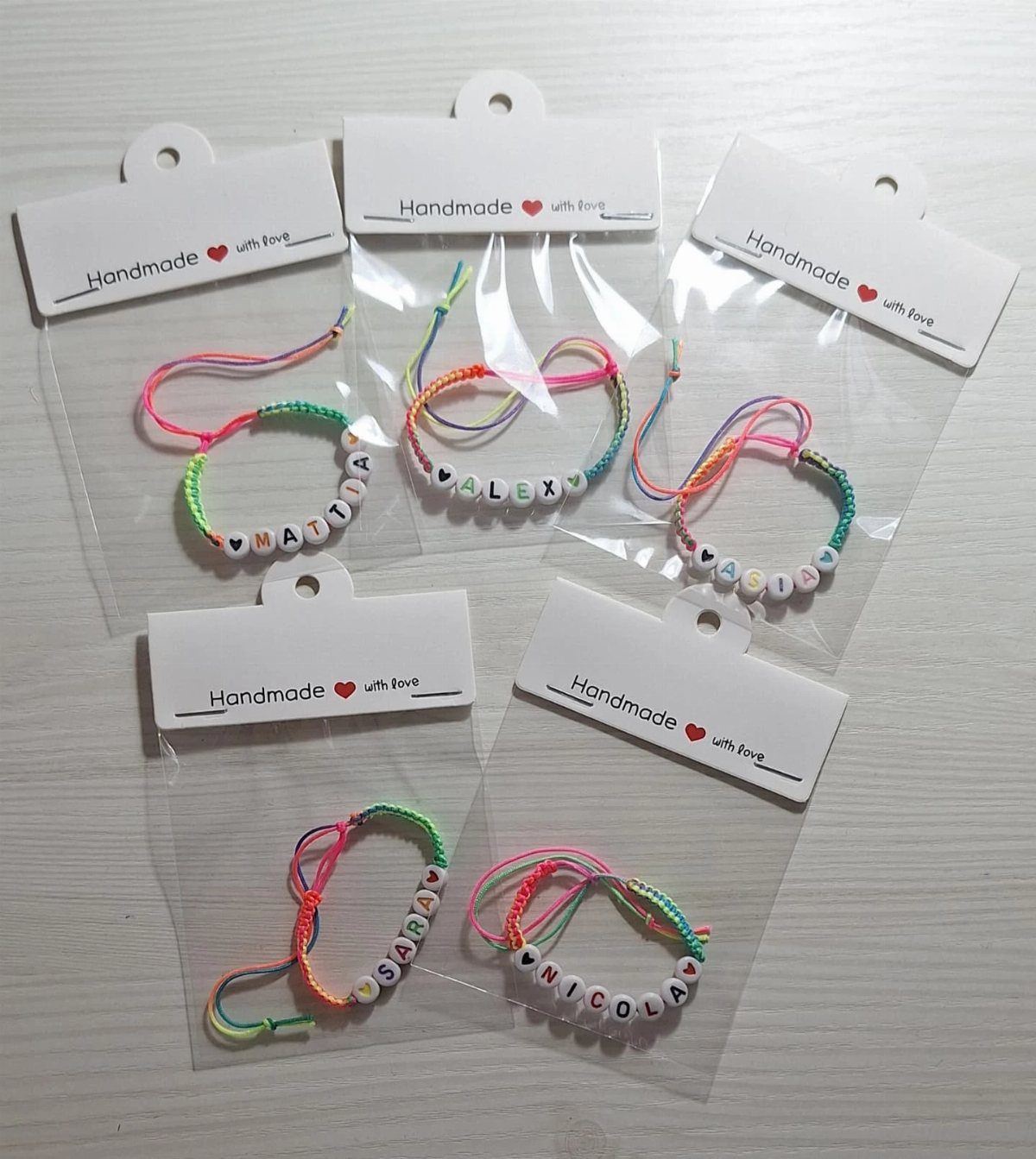 Colorful braided friendship bracelets with name beads in clear plastic packaging.