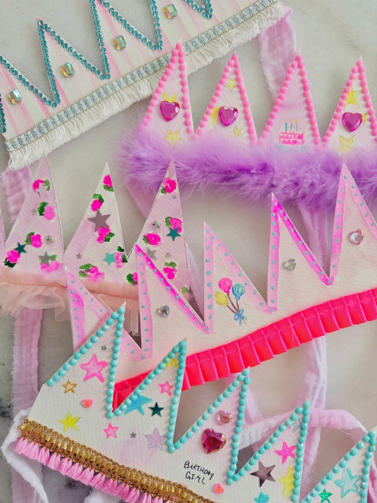 Handmade paper birthday crowns decorated with glitter, stars, and pink heart gems.