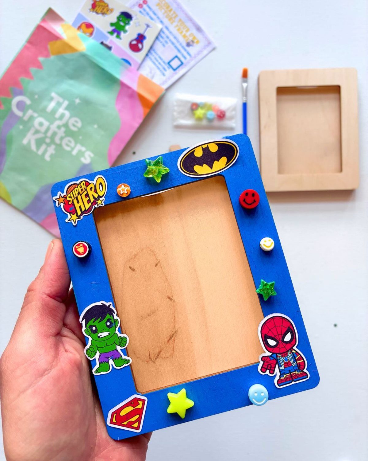 Blue wooden picture frame decorated with superhero stickers and colorful plastic shapes.