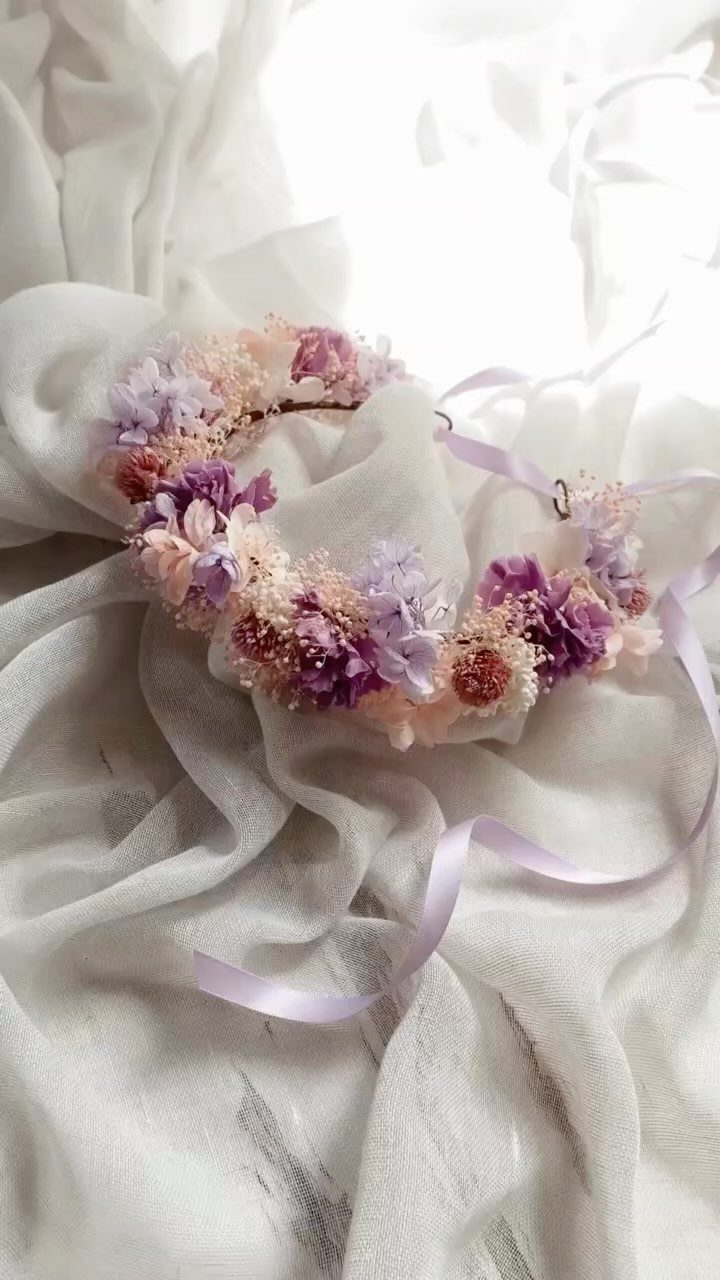 Floral crown with pink and purple flowers resting on white draped fabric.