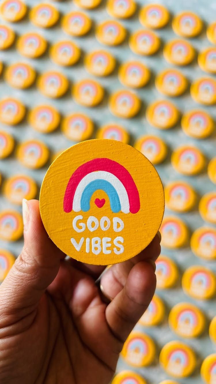 Yellow painted rock with a rainbow and 'GOOD VIBES' text held by hand.