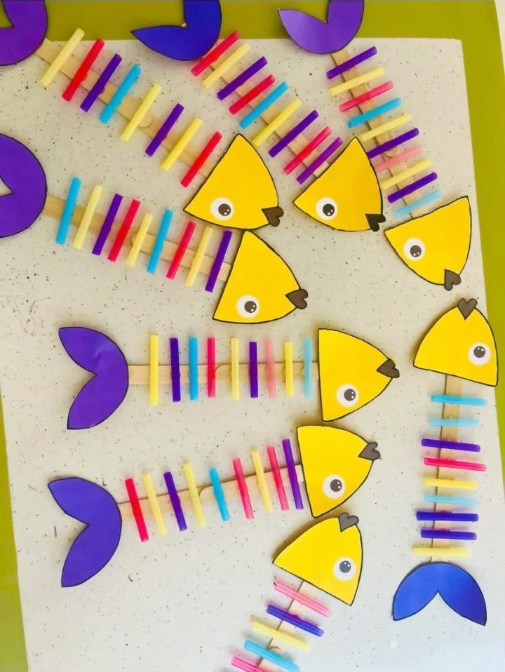 Colorful fish crafts made from popsicle sticks, yellow paper heads, and purple tails.