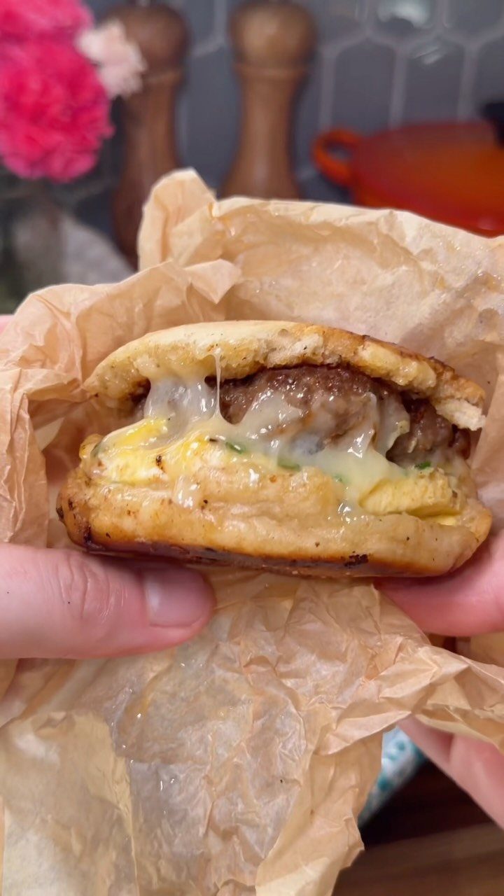 Breakfast sandwich with sausage, egg, and cheese on a toasted biscuit in parchment paper.
