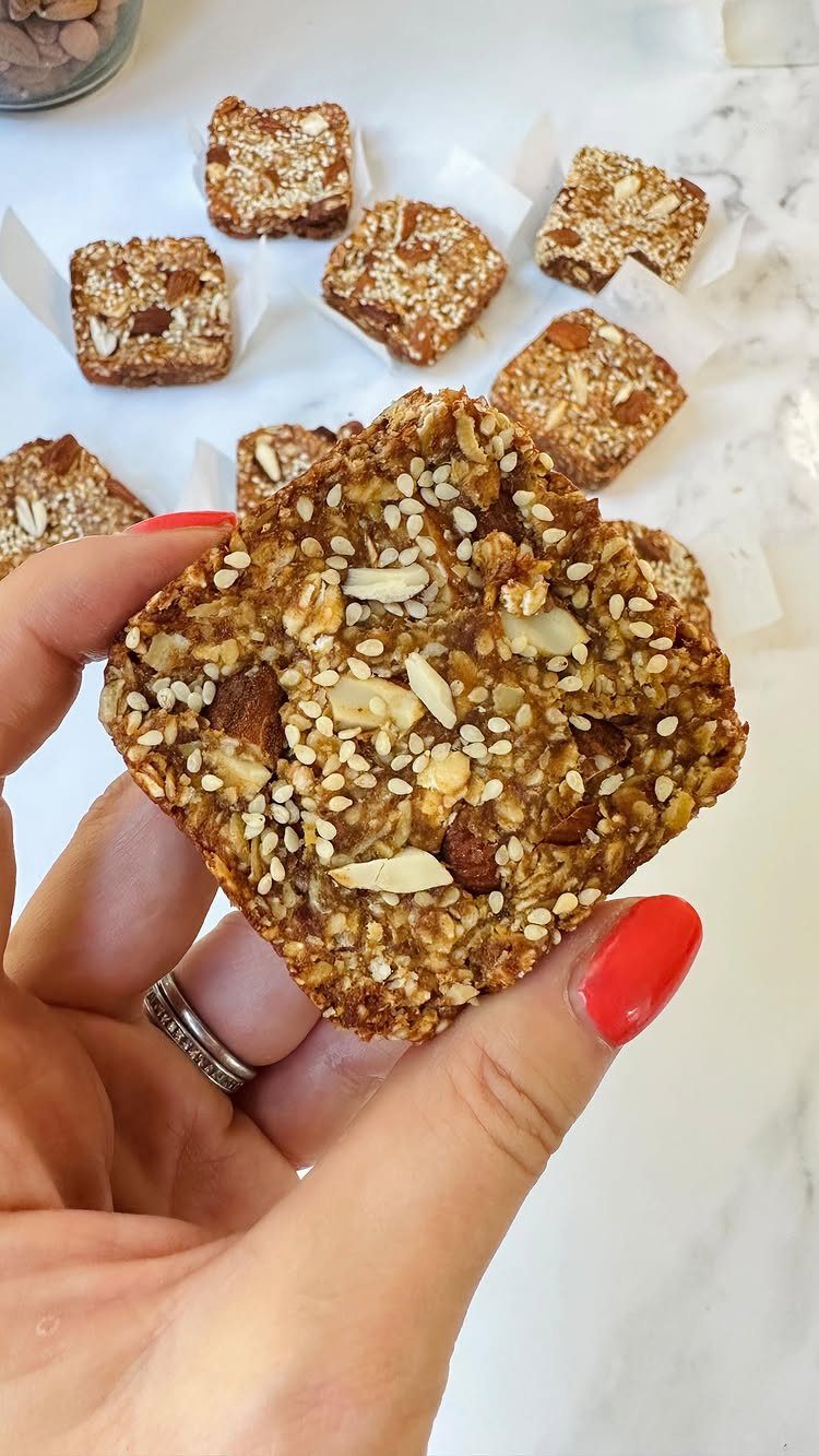 Granola bar held by a hand with red nails over a marble surface.
